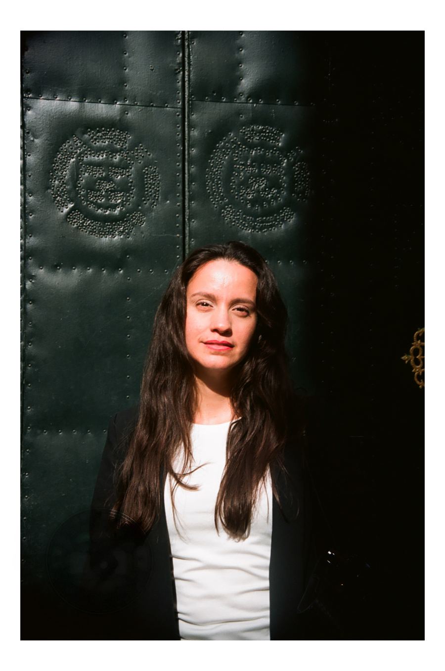 Retrato de una mujer ante un port&oacute;n verde de metal remachado, con la luz cruzada del sol
