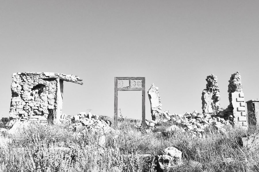 Restos de muros de piedra y el marco de una puerta en pie sobre un campo de hierba seca
