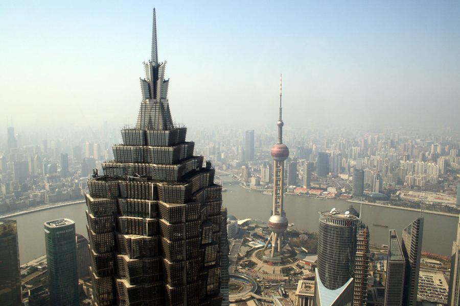 **Vertical Shanghai**

Desde las alturas de Pudong, Shanghái se extiende hasta perderse en la bruma. La Torre Jin Mao domina el primer plano mientras la Oriental Pearl emerge frente al Huangpu, rodeada por una ciudad que parece no tener límite. La imagen retrata un momento de transformación: una metrópolis creciendo en vertical, suspendida entre la niebla, el río y una ambición arquitectónica casi infinita.
