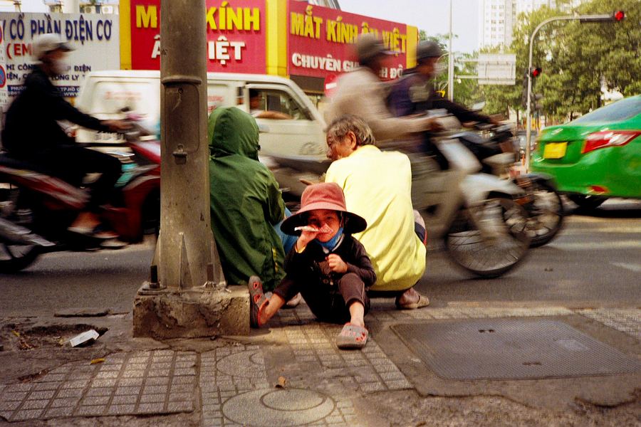 Una escena de vida cotidiana atrapada en medio del caos urbano. Mientras motocicletas y vehículos atraviesan la imagen convertidos en movimiento, un niño permanece sentado en primer plano, ajeno al ritmo frenético que lo rodea. La fotografía juega con el contraste entre quietud y velocidad, creando una imagen directa y humana sobre la infancia, la calle y esos pequeños instantes que pasan desapercibidos dentro de la ciudad.